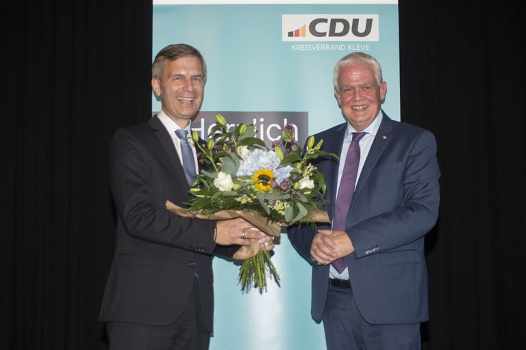 Zwei Herren in Anzügen überreichen sich bei CDU-Veranstaltung Blumen mit herzlichem Händedruck.